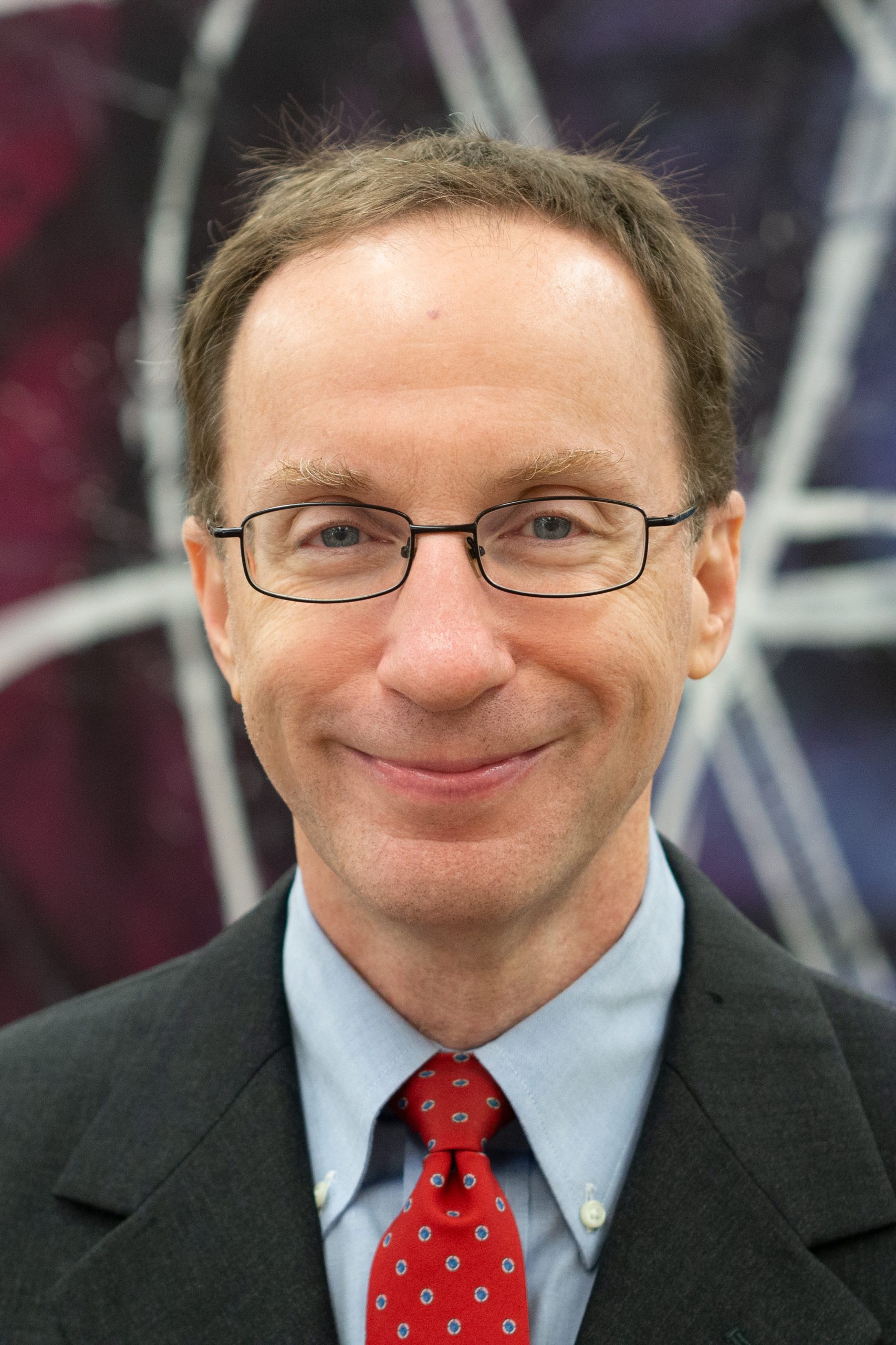 A photo of Richard Gerrig in a dark suit and red tie